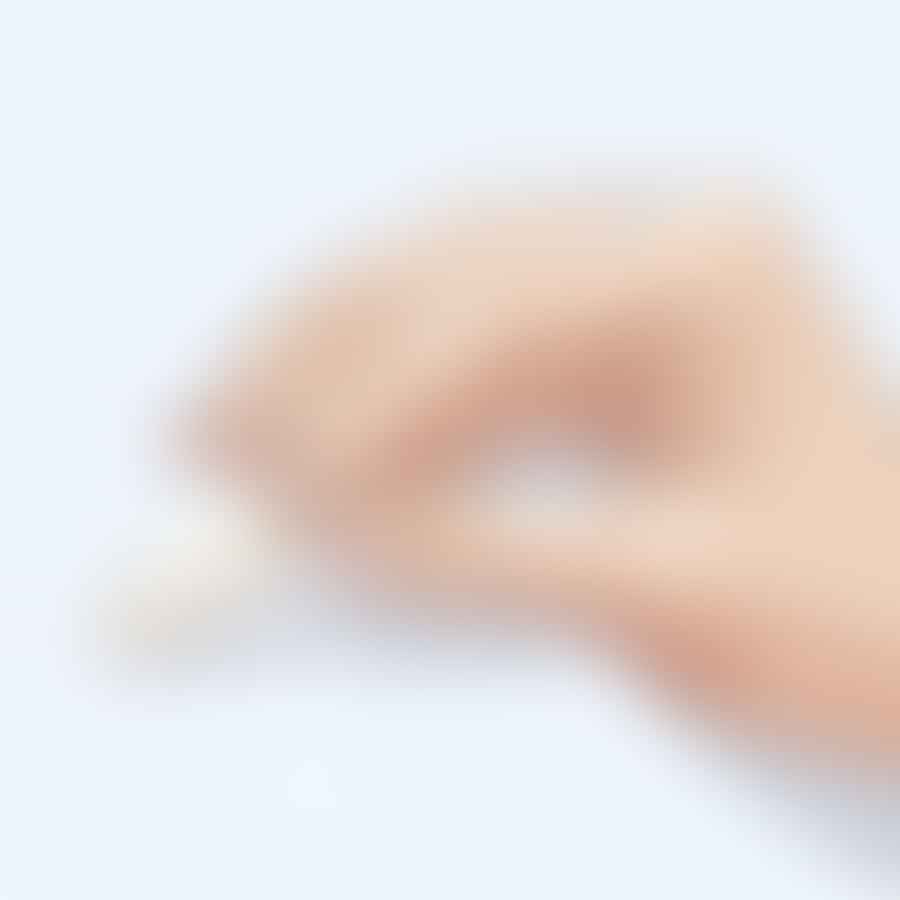 A hand applying a clear top coat to white almond-shaped nails.