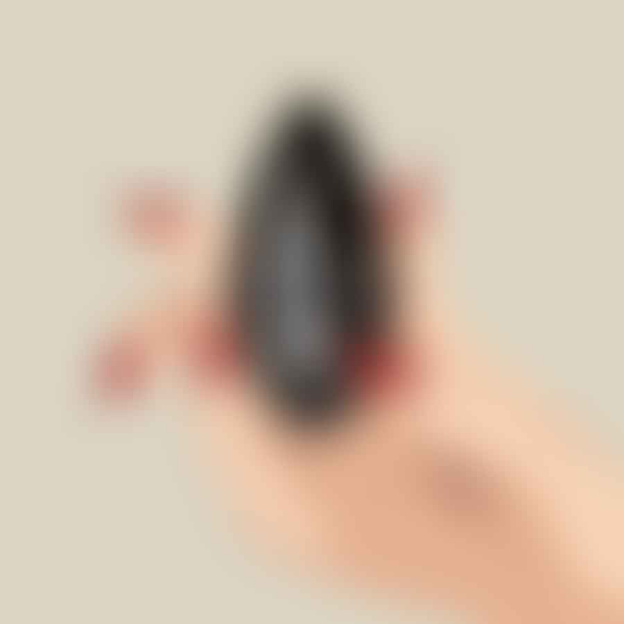 A hand applying a clear top coat on a black-painted almond-shaped nail with a white spiderweb and spider design.